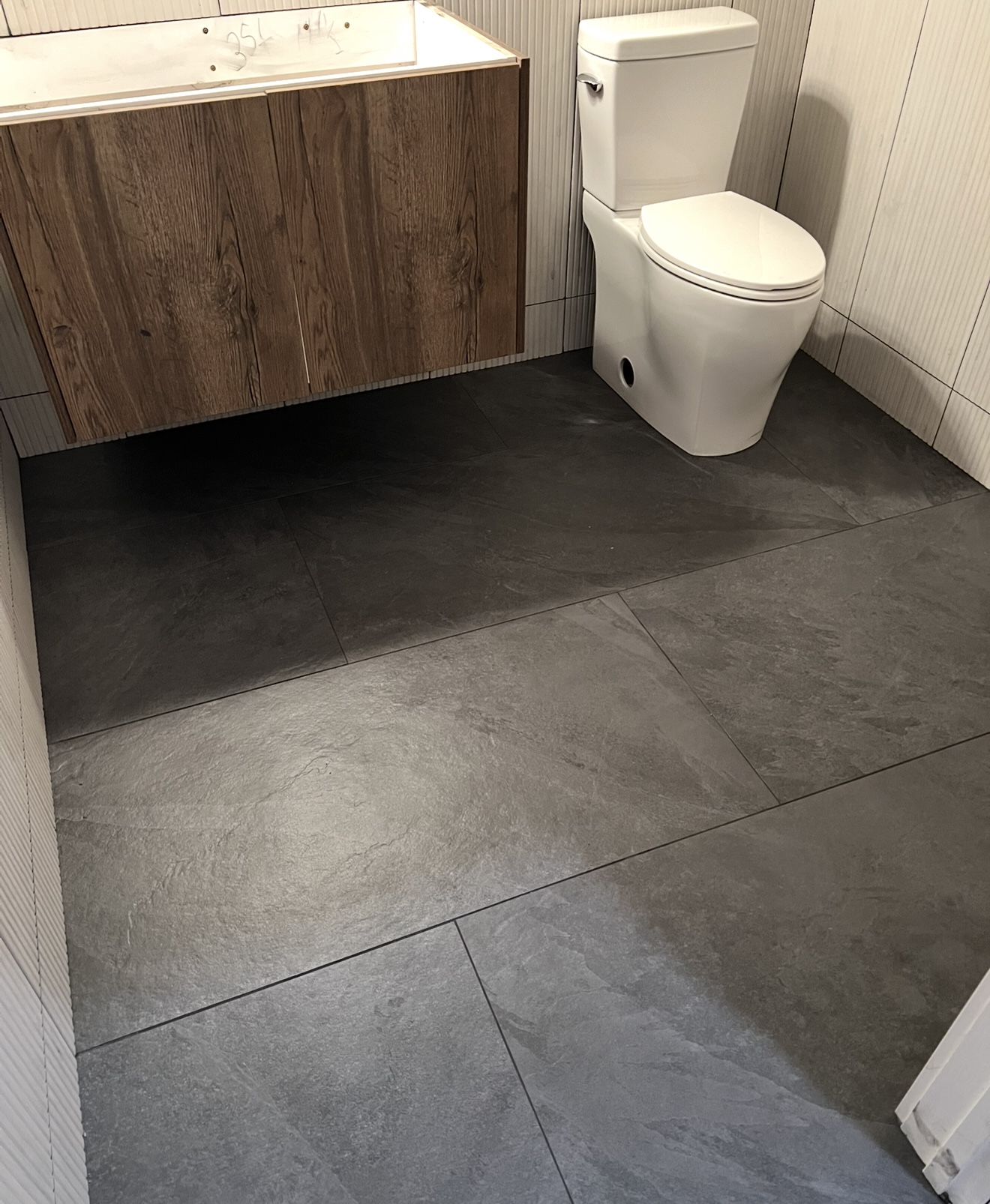 Modern bathroom with dark grey tile flooring, floating wood vanity, and fluted white walls