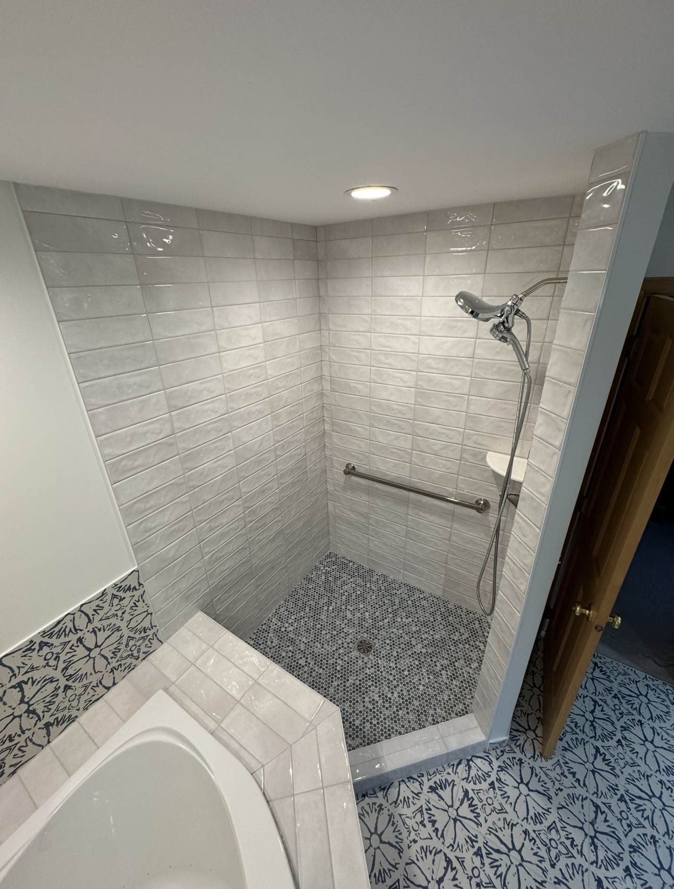 Bathroom with walk-in shower, light gray subway tile walls, dark penny tile shower floor, navy floral patterned floor tile, and tub with matching accent backsplash