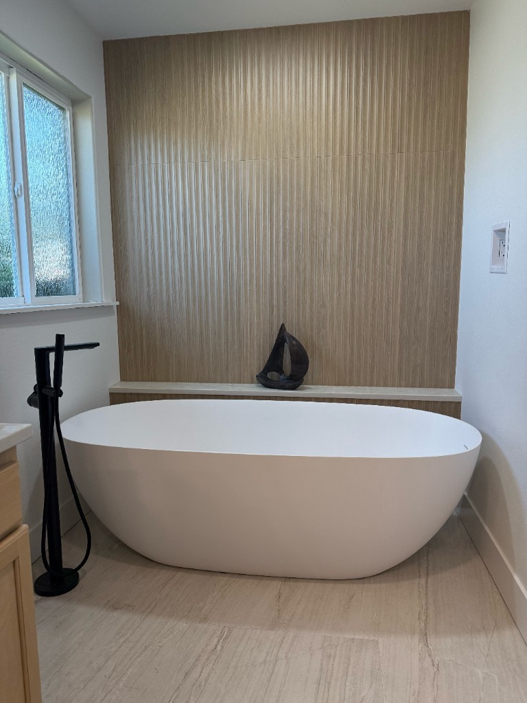 Freestanding bathtub with fluted wood accent wall and light tile flooring