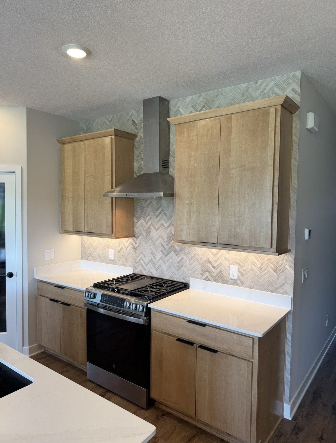 Modern kitchen with light wood cabinetry, full-height herringbone tile backsplash, white quartz countertops, and stainless steel range and hood