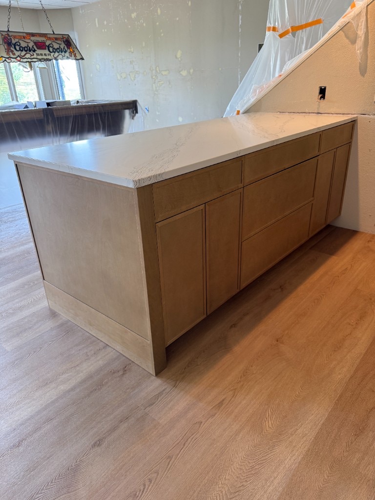 Kitchen or bath island cabinet install with light wood cabinetry, white marble-look countertop, and wood-look LVP flooring during remodel