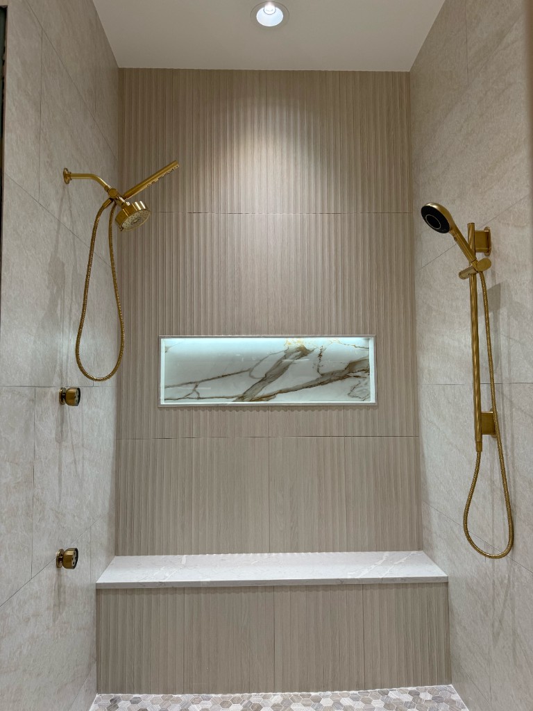 Luxurious walk-in shower with gold fixtures, fluted tiles, marble niche, and hexagonal mosaic floor