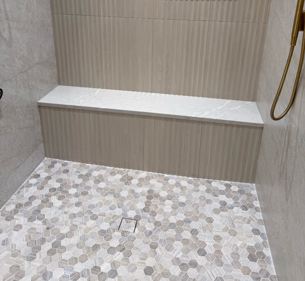 Custom tile shower with fluted wall tile, marble niche, and hexagonal mosaic floor